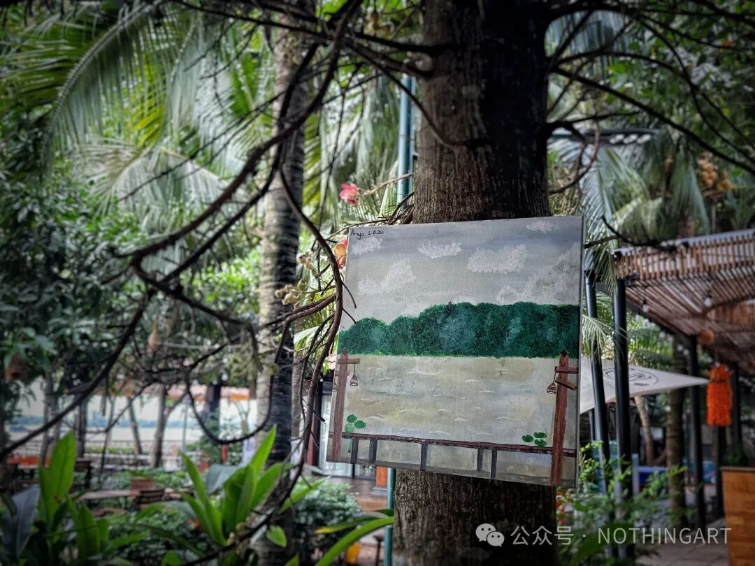 一幅描绘河流、远处绿树与近处栏杆的画作悬挂于枝叶间的树干上。