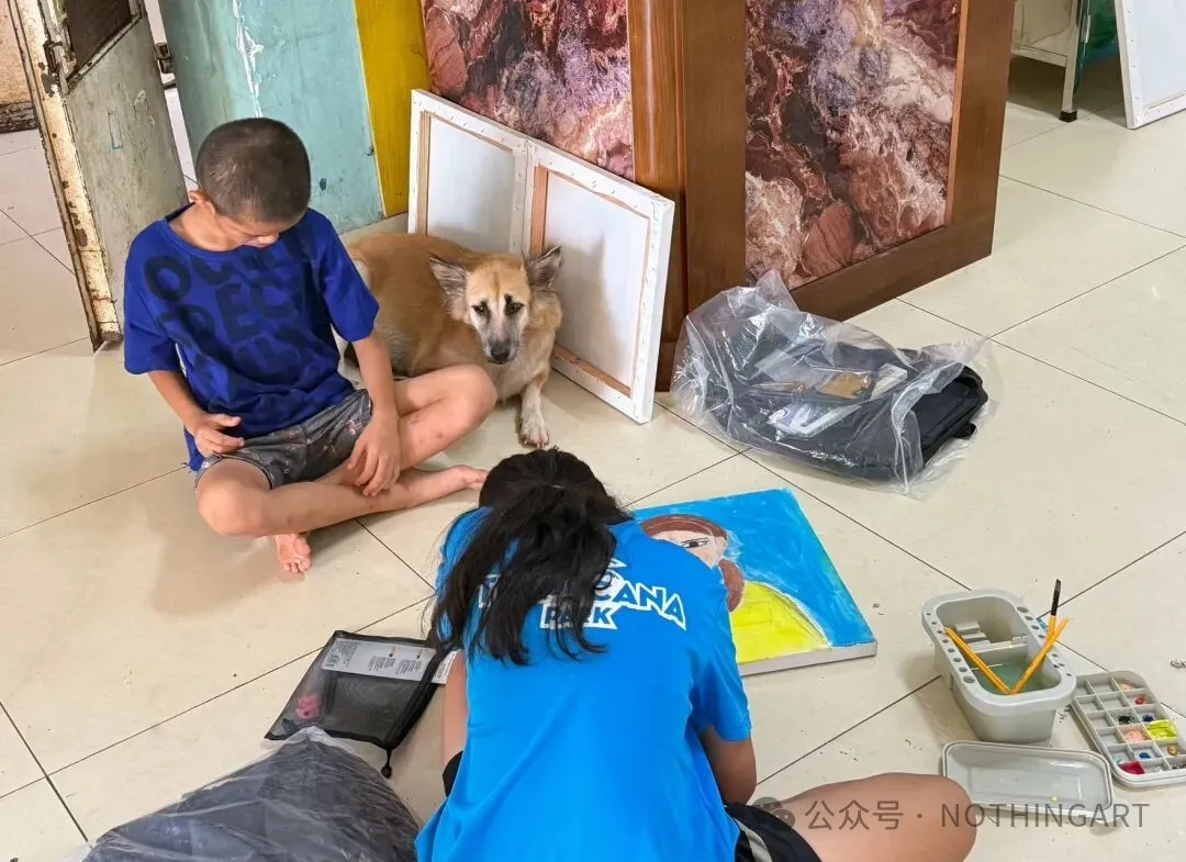 A participant paints a portrait on the floor while another participant and a dog sit nearby.